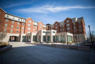 The rear of the Lewis Honors College and Lewis Hall, showing the two buildings' interconnectedness. The sky is clear and blue. A lone student walks past the courtyard of the Lewis Honors College.