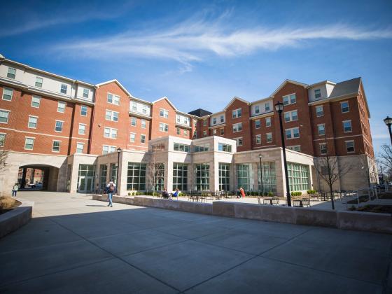 The rear of the Lewis Honors College and Lewis Hall, showing the two buildings' interconnectedness. The sky is clear and blue. A lone student walks past the courtyard of the Lewis Honors College.