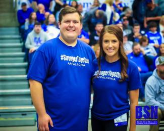Two people in blue Appalachian Health Initiative (AHI) t-shirts in front of a stadium of UK fans and students.
