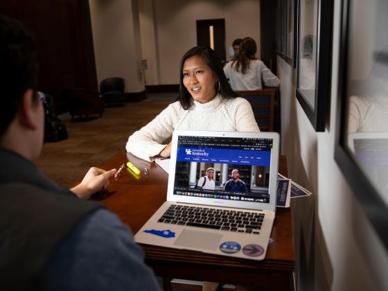 Lewis Honors staff and student talking while one has a laptop open, displaying the Lewis Honors webpage.